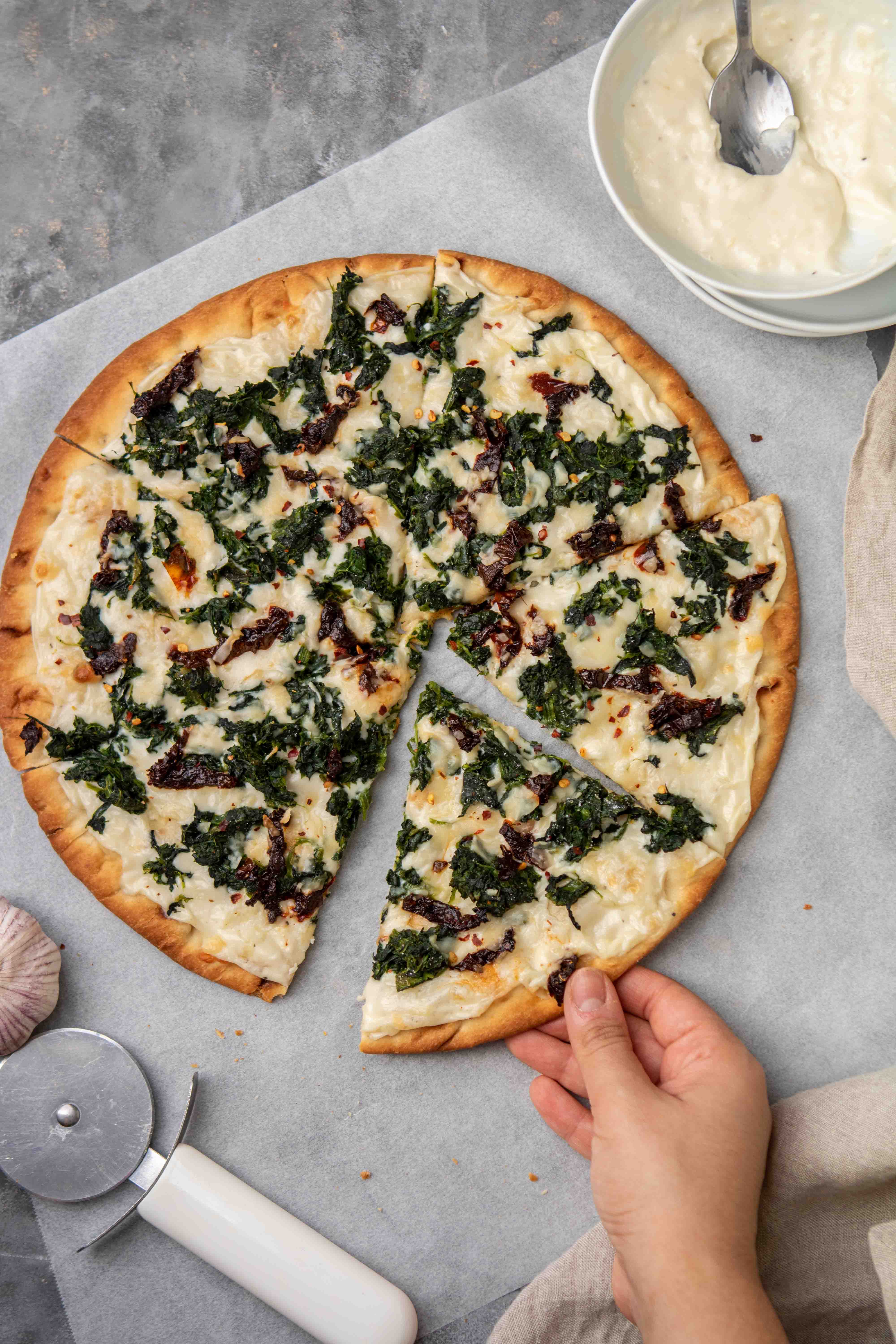 Main attrapant une tranche de pizza à la sauce blanche