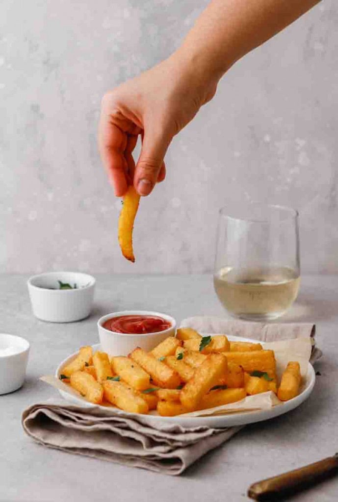 Main trempant une frite de polenta dans le ketchup